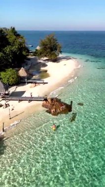 Explore a breathtaking beach in Thailand featuring crystal-clear waters and soft white sand. Visitors enjoy the serene environment, surrounded by lush greenery and an inviting atmosphere.