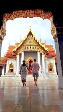 Bir çift el ele yürür Tayland 'da güzel bir tapınağın büyük girişine doğru. Bangkok 'taki Benchamabophit Tapınağı