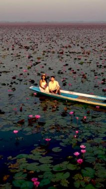 Bir çiftin Tayland, Udon Thani 'deki büyüleyici nilüfer çiçekleri tarlasında sakin bir tekne yolculuğunun tadını çıkardığı huzurlu bir anı yaşayın. Kırmızı Lotus Gölü