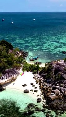 Canlı turkuaz sular, Tayland 'da yemyeşil ve engebeli kayalarla çevrili beyaz kumlu sahilde nazikçe tur atar. Ufukta küçük tekneler Koh lipe 'de parlak bir gökyüzünün altında bekliyor.