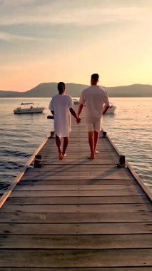 Romantik bir an başlıyor. Tayland 'da sakin bir ahşap iskele boyunca el ele yürüyen bir çift gibi. Güneş arka planda batar, sıcak renklerle gökyüzünü boyarken, tekneler yavaşça süzülür..