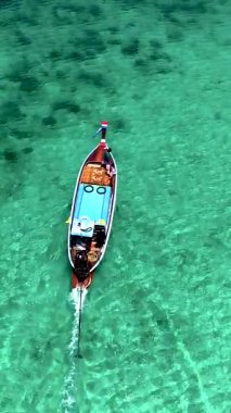 Geleneksel bir uzun kuyruklu tekne, Tayland 'ın berrak turkuaz sularında süzülerek tropikal manzaranın çarpıcı güzelliğini gözler önüne seriyor..