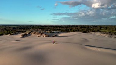 Danimarka 'daki Rabjerg Mile' ın nefes kesici güzelliğini keşfedin. Yumuşak kum tepeciklerinin açık mavi gökyüzüne doğru uzandığı yer. İki insan huzurlu manzarada yürür, doğanın huzurunun tadını çıkarırlar..