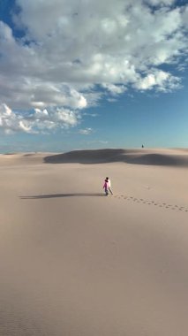 İki insan, Danimarka 'daki Rabjerg Mile' ın yumuşak, kumlu kum tepelerinde kabarık bulutlu parlak mavi bir gökyüzünün altında el ele dolaşarak barışçıl ve canlandırıcı bir atmosfer yaratıyor..