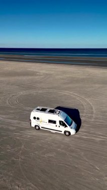 Danimarka 'nın Romo Adası Lakolk Strand şehrinde huzurlu bir manzara gözler önüne seriliyor. Bir karavan kumlu sahilde, çarpıcı bir mavi gökyüzünün altında sükunet dalgalarıyla kıyıya doğru ilerliyor..