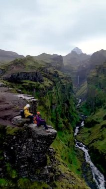 İzlanda 'daki büyüleyici Mulagljufur Kanyonu' na tanık olun. Maceracılar engebeli kayalıkların tepesinde dinleniyor. Bereketli yeşil manzara ve akan nehir keşif için pitoresk bir zemin oluşturur.