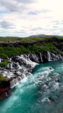 Hraunfossar Şelalesi 'nin nefes kesici güzelliğini deneyimleyin. Kristal berraklığında suyun bereketli yeşilliklerle çevrili lav oluşumları üzerinde zarafetle aktığı yer. Doğaya huzurlu bir kaçış..