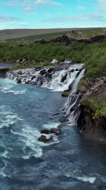 Hraunfossar Şelalesi gözenekli lav kayalarının üzerinden akan suları sergiliyor, büyüleyici bir görüntü yaratıyor..
