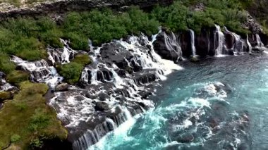 Göz kamaştırıcı Hraunfossar şelalesine hayret, kristal berrak su lav kayaları üzerinde dalgalanarak canlı turkuaz havuzlara dönüşüyor. İzlanda 'nın nefes kesici doğal güzelliğini tecrübe et..