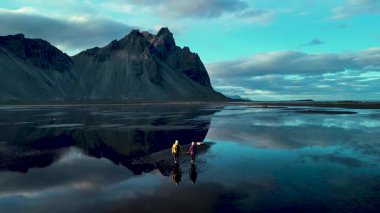 İki maceracı, çarpıcı Stoksnes Vestrahorn kıyı şeridi boyunca yürüyor. Etrafı dramatik dağlar ve parıldayan sularla çevrili. İzlanda kıyı şeridinin doğal güzelliğini tecrübe edin..