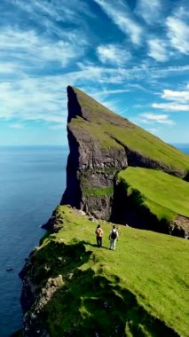Yürüyüşçüler Faroe Adaları 'nda okyanusa bakan dramatik uçurumlarda duran büyüleyici Mylingur patikalarını keşfediyorlar. Parlak yeşil manzara mavi gökyüzü ile çok güzel tezat oluşturuyor..