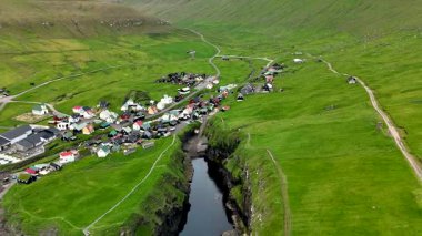 Gjogv köyü, Faroe Adaları 'nın canlı yeşil tepelerine kurulmuştur. Manzara engebeli uçurumları ve akan suları sergiliyor, sakin bir atmosfer yaratıyor..