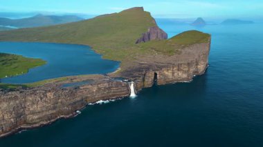 Faroe Adaları 'ndaki Sorvagsvatn Gölü' nün çarpıcı güzelliğini keşfedin, dramatik uçurumlar ve çağlayan bir şelale gösterin. Sakin sular, berrak bir gökyüzünün altındaki canlı manzarayı yansıtır..