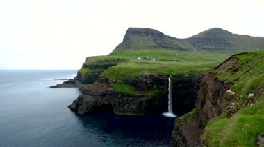 Gasadalur köyü yakınlarındaki okyanusa akan Mulafossur şelalesinin çarpıcı güzelliğini görün. Bereketli yeşil kayalıklar ve sakin sular büyüleyici bir manzara yaratır..