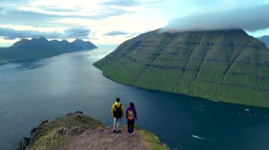 İki yürüyüşçü Klakkur Faroe Adaları 'nın nefes kesici manzarasına bakar. Yükselen uçurumlar sakin sularla karşılaşıyor, sakin bir gündüz keşfi sırasında güzellikleri gözler önüne seriyor..