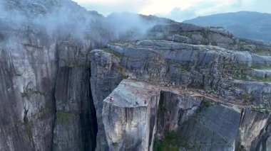 Norveç 'in Preikestolen kentinin göz kamaştırıcı manzarasına tanık olun, burada yüksek uçurumlar aşağıdaki dingin fiyortla buluşuyor. Yürüyüşçüler şafağın altın ışığında bu doğa harikasına hayret eder..