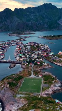 Henningsvaer futbol stadyumunun göz kamaştırıcı hava manzarasını keşfedin. Lofoten 'ın muhteşem arka planına karşı. Canlı yeşil zemin kıyı manzarası ve büyüleyici köyle çelişiyor..