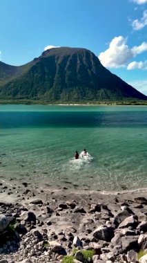 İki birey, dramatik dağlar ve parlak mavi gökyüzü ile çevrili Lofoten 'in berrak sularına serinletici bir dalışın tadını çıkarıyor. Bu pitoresk yer doğaya mükemmel bir kaçış sunuyor..