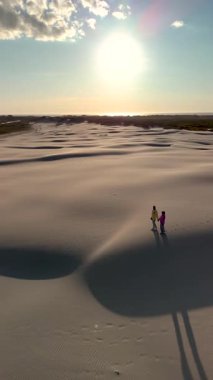 Danimarka 'daki Rabjerg Mile' da kum tepeleri uzanıyor. İki birey, ılık bir günbatımı parıltısıyla aydınlanan yumuşak kumda yürürler, dingin ve büyüleyici bir atmosfer yaratırlar..