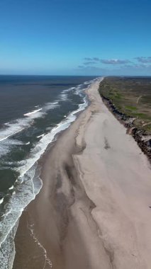 Danimarka 'da Rubjerg Knude deniz feneri yakınlarındaki büyüleyici manzarayı keşfedin. Altın kumların parıldayan okyanusla buluştuğu yer. Dalgalar yavaşça kıyıya vurur berrak mavi gökyüzünün altında.