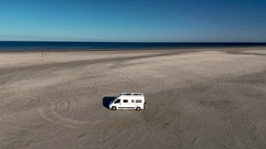 Danimarka, Romo 'daki Lakolk Strand plajının sakin manzarasında kumlu sahilde park etmiş beyaz bir karavan var..