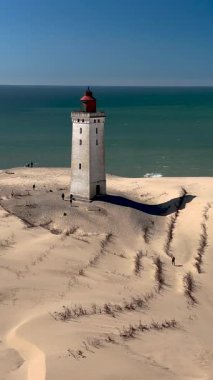 Muhteşem Rubjerknudde deniz fenerini keşfedin Danimarka 'nın rüzgârlı sahil şeridindeki altın kum tepeleri arasında dimdik ayakta durun. Çarpıcı yapı turkuaz denizle çok güzel zıtlaşıyor..