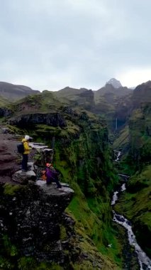 İzlanda 'da, Mulagljufur Kanyonu' nda dramatik uçurumlar, yemyeşil alanlar ve akan nehirler sergilenir. İki yürüyüşçü karamsar gökyüzünün altındaki görkemli manzaraya hayran, doğaları merak ediyor..