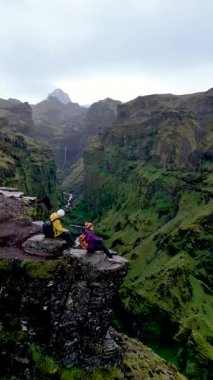 Maceracılar İzlanda 'daki Mulagljufur Kanyonu' nun kıyısından çarpıcı manzaraları izliyorlar. Etrafı yemyeşil uçurumlar ve aşağıdaki kıvrımlı bir nehirle çevrili dramatik manzara sanatsal özellikler sergiliyor..