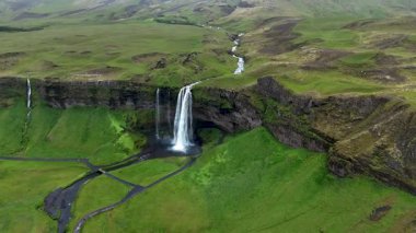 Seljalandsfoss şelalesini keşfedin, suyun zarif bir şekilde yeşil bir vadiye düştüğü yeri. Bu nefes kesici İzlanda manzarasında doğanın ihtişamı gözler önüne seriliyor..