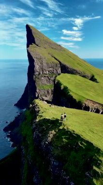 Güneşli bir günde okyanusa bakan dik uçurumları aşan yürüyüşçülerin olduğu Faroe Adaları 'ndaki Mylingur' un güzelliğini deneyin. Panoramik manzaraların ve canlı yeşil manzaraların tadını çıkarın..