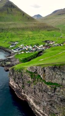Faroe Adaları 'ndaki yemyeşil tepeler ve dramatik uçurumların arasında yuva yapmış Gjogv köyünün cazibesini keşfedin. Huzurlu sular, evlerin canlı renklerini yansıtarak, huzurlu bir atmosfer yaratıyor..