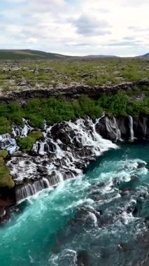 İzlanda 'daki çarpıcı Hraunfossar şelalesini keşfedin. Temiz sular lav kayalarının üzerinden canlı turkuaz havuzlara akar, yemyeşil ve nefes kesici manzaralarla çevrilidir..