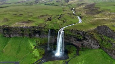 İzlanda 'daki Seljalandsfoss şelalesinin nefes kesici güzelliğini tecrübe edin. Yükseklerden suyla zarif bir şekilde dalış yapan, yemyeşil tepeler ve manzara manzaralarıyla çevrili. Gerçek bir doğal mucize.