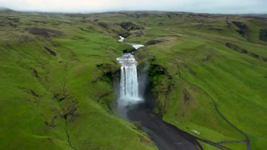 İzlanda 'da büyüleyici bir doğa harikası olan Skogafoss Şelalesi' nin hayranlık uyandıran güzelliğini tecrübe edin. Su, canlı yeşilliklerle çevrili kayalıkların üzerinden güçlü bir şekilde akar..