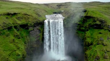 İzlanda 'daki nefes kesici Skogafoss şelalesine tanık olun. Sarp kayalıklardan güçlü bir şekilde akıyor. Parlak yeşil manzara bu doğal harikayı çevreleyip sakin bir atmosfer yaratıyor..
