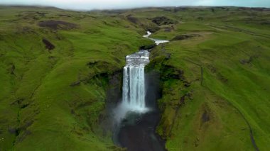 İzlanda 'daki Skogafoss Şelalesi' nin nefes kesici güzelliğini tecrübe edin. Su, canlı yeşil tepeler ve sakin bir atmosferle çevrili kayalıklardan güçlü bir şekilde düşer. Gerçek bir doğal mucize bekliyor..