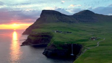 Güneş Mulafossur şelalesi üzerinde batarken Gasadalur köyü yakınlarındaki okyanusa dökülen Faroe Adaları 'nın nefes kesici güzelliğini deneyimleyin..