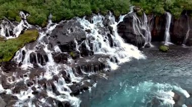 Hraunfossar şelalesinin büyüleyici akışına tanık olun kristal berrak su çağlayanı gibi kayalık oluşumlar üzerinde yemyeşil ile çevrili. İzlanda 'nın eşsiz güzelliğini keşfedin..