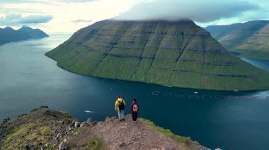 Yürüyüşçüler Klakkur Faroe Adaları 'ndaki bir uçurumun muhteşem manzarasının keyfini çıkarıyorlar. Dramatik manzara yemyeşil dağlar ve sakin mavi bir denizi barındırır. Doğa güzelliğine mükemmel bir kaçış..