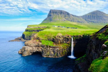Gasadalur Şelalesi kayalık kayalıklardan Atlantik Okyanusu 'na yuvarlanırken. Yazın Mulafossur ve Gasadalur Köyü, Faroe Adaları