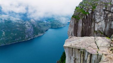Norveç 'teki Lysefjord' un sakin sularının üzerinde dramatik uçurumlar yükselir. Yeşillik yemyeşil bulutlu bir gökyüzünün altındaki görkemli kaya oluşumlarıyla çelişiyor. Macera arayanlar ve doğa severler için mükemmel..