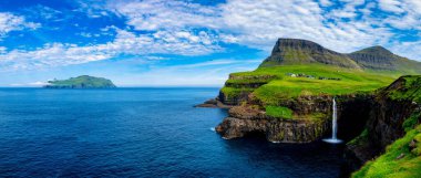 Gasadalur Şelalesi kayalık kayalıklardan Atlantik Okyanusu 'na yuvarlanırken. Mulafossur ve Gasadalur Köyü, Faroe Adaları