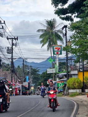 Koh Chang, Tayland, 30 Ekim 2025, sakinler, dükkanların ve palmiye ağaçlarının yol boyunca 711 işareti olan caddelerde geziniyorlar.