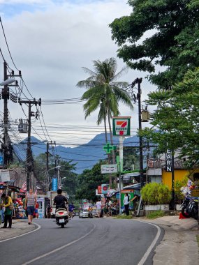 Koh Chang, Tayland, 30 Ekim 2025. Renkli dükkanlar işlek yollar boyunca uzanıyor. Motosikletler bulutlu gökyüzünün altında sallanırken vızıldıyor, ziyaretçiler ve yerel halk için davetkar bir atmosfer yaratıyor.