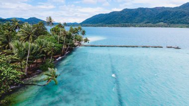 Phrao Nok Adası 'nda çarpıcı turkuaz sular, rüzgarda hafifçe sallanan palmiye ağaçları ve arka planda resim gibi dağlar sergilenmektedir. Koh Chang Tayland