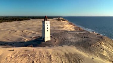 Danimarka 'nın kumlu kumulları arasında dimdik duran çarpıcı Rubjerknudde deniz fenerini keşfedin. Altın saat, kıyı şeridi boyunca güzel gölgeler bırakır. Huzuru ve yansımayı davet eder..