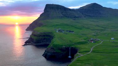 Faroe Adaları 'ndaki canlı günbatımında Gasadalur köyünün freskli zeminine vuran Mulafossur şelalesinin okyanusa dökülüşünün çarpıcı güzelliğini deneyimleyin..
