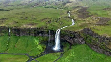 İzlanda 'nın engebeli kayalıklarından dökülen görkemli Seljalandsfoss şelalesine tanık olun. Bereketli yeşillik bölgeyi çevreleyerek sakin bir atmosfer yaratıyor..