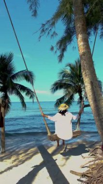 Koh Kood Adası 'nda sakin bir an. Bir kadın, ahşap bir salıncakta sallanıyor. Berrak palmiyelerin arasında.