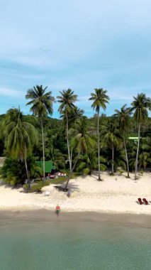 Tayland 'da Koh Kood Adası, yumuşak beyaz kumların kristal berrak sularla buluştuğu yer. Tomurcuk gibi sallanan palmiye ağaçları, ziyaretçiler gibi sıcak güneşin tadını çıkarırlar, sahilde salıncakta sallanan bir çift.